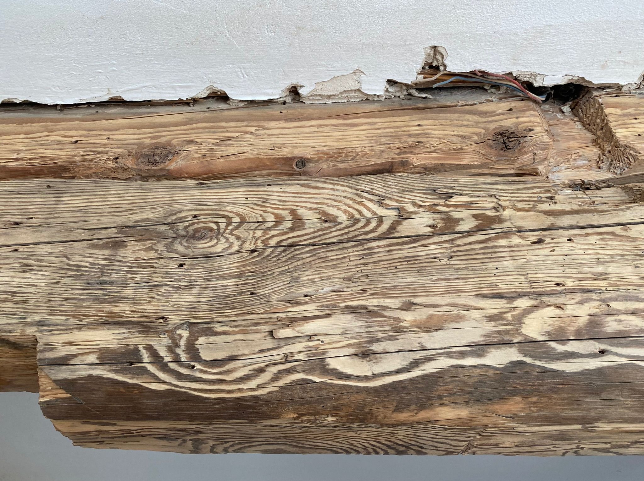 Uszkodzona belka stropowa z widocznymi śladami po instalacji elektrycznej i odpadającym tynkiem.