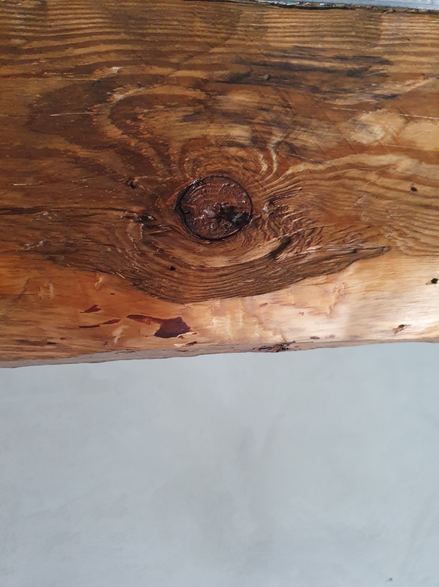 Fragment drewnianej belki stropowej z wyraźnym sękiem i widocznym usłojeniem, na tle jasnej ściany.