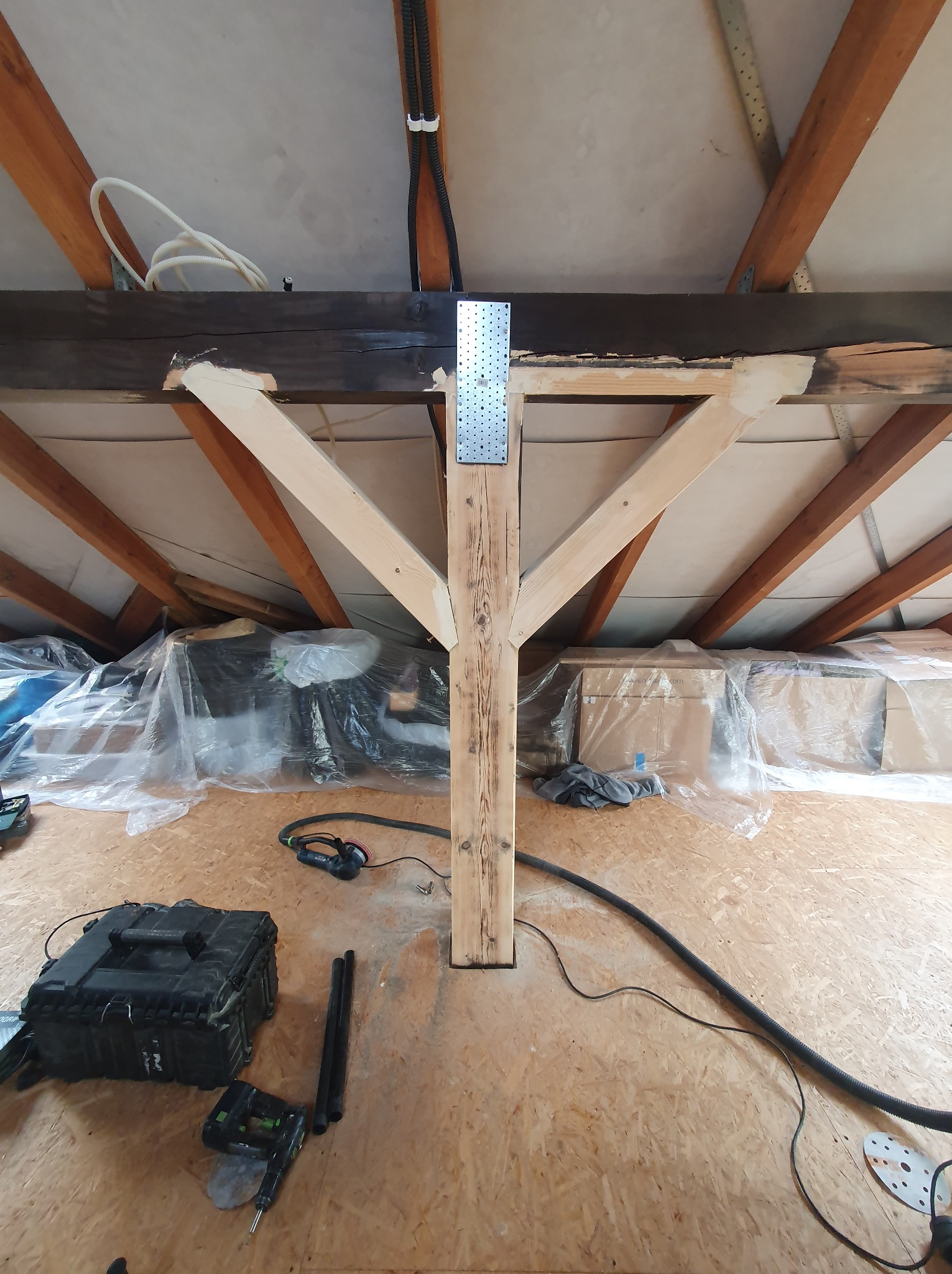 Wiązary dachowe w trakcie montażu w Krakowie, widoczny drewniany słup wzmacniający z metalowym łącznikiem, narzędzia i osłonięte folią elementy konstrukcyjne.