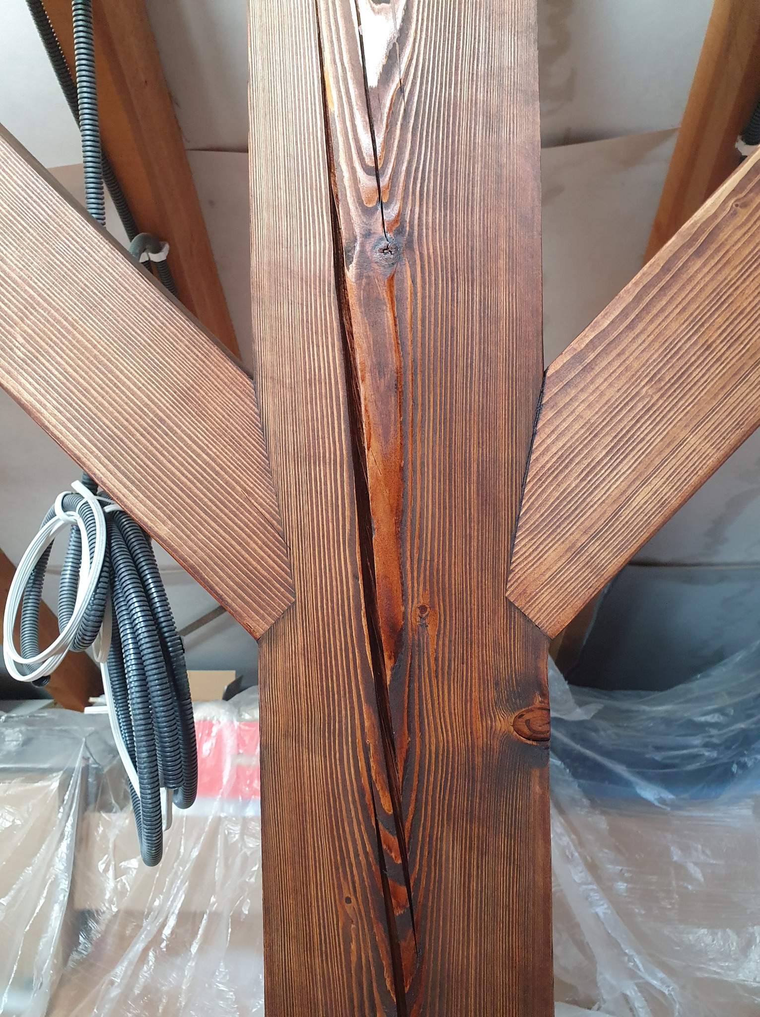 Fragment drewnianej konstrukcji dachu z widocznymi elementami więźby, zabezpieczonymi folią i przewodami elektrycznymi.