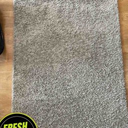 Fresh Clean - Wyprany, puszysty, szary dywan typu shaggy leżący na drewnianej podłodze, z widocznym napisem 'FRESH CLEAN Po' w rogu.