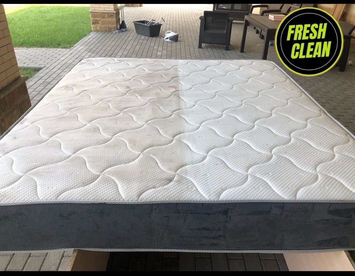 Materac z widoczną różnicą przed i po czyszczeniu, z lewej strony zabrudzony, z prawej czysty, na tle kostki brukowej i zieleni.