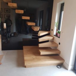 Drew Max - Nowoczesne schody wspornikowe z drewna dębowego, mocowane do ściany z czarnego szkła, z widocznymi odbiciami osób i narzędzi