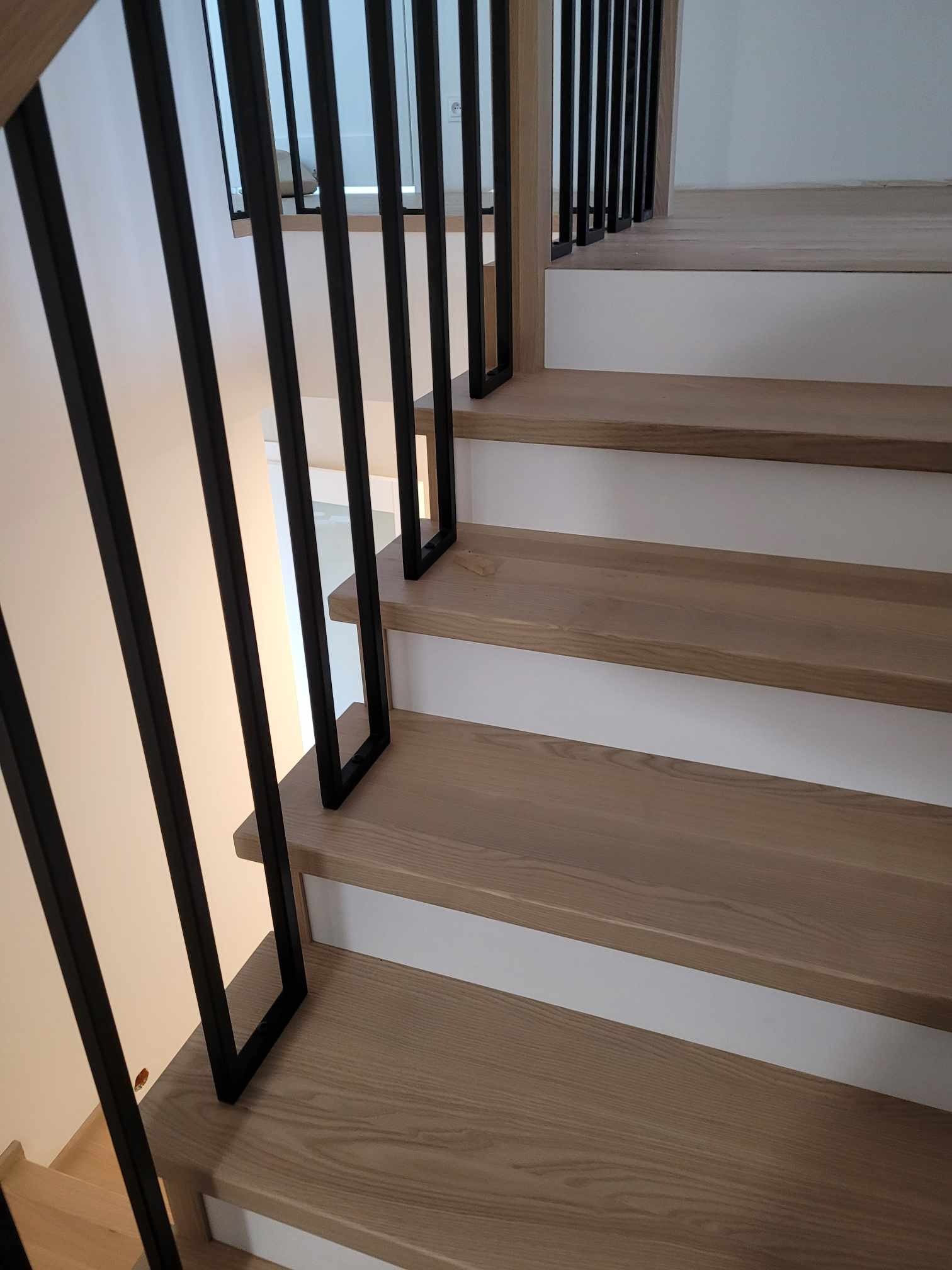 Schody drewniane z białymi podstopnicami i czarną, minimalistyczną balustradą metalową, widok z dołu.