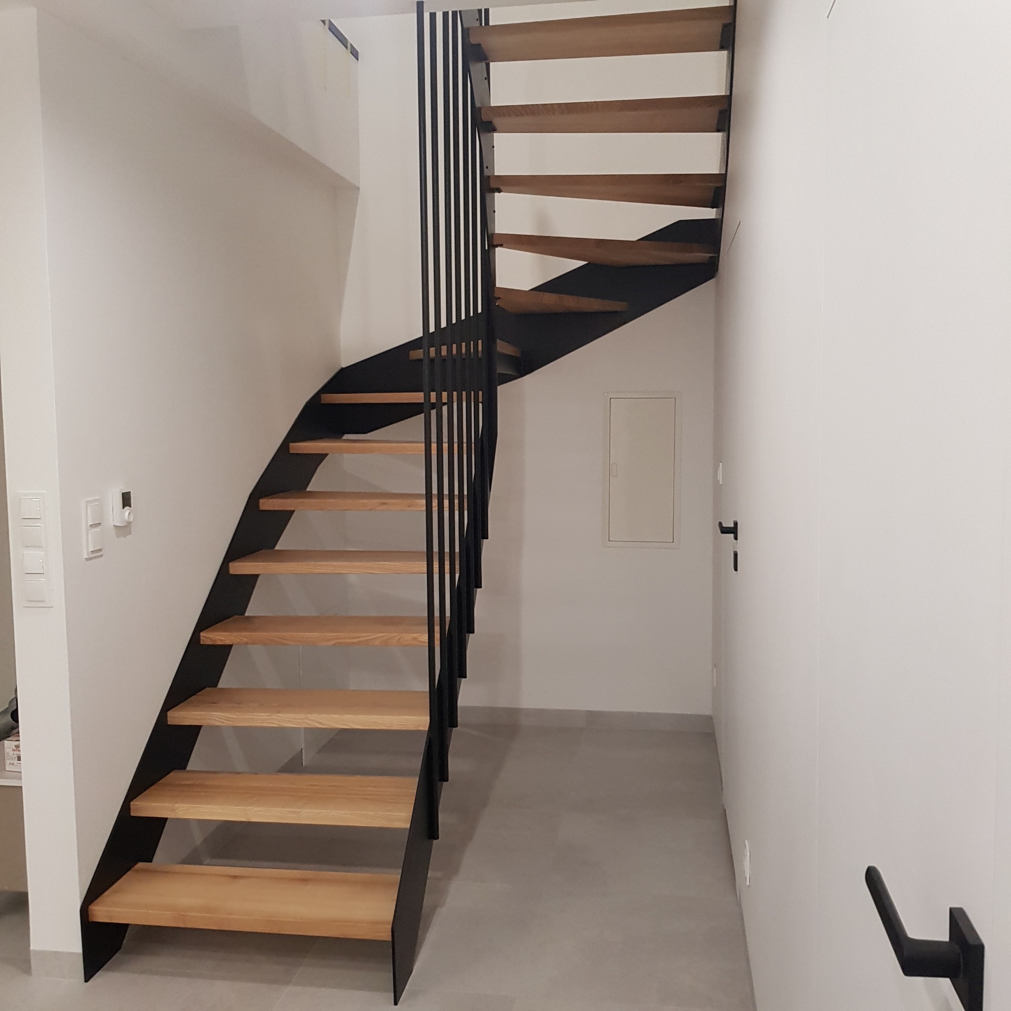 Nowoczesne schody z drewnianymi stopniami i czarną metalową konstrukcją, widok z dołu, minimalistyczne wnętrze.