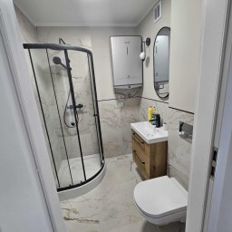 Małgorzata Grzesik MAL - BUD - Wykończona łazienka z kabiną prysznicową typu walk-in z czarnymi ramami, umywalką z drewnianą szafką i marmurową podłogą. Widok zza uchylonych drzwi.