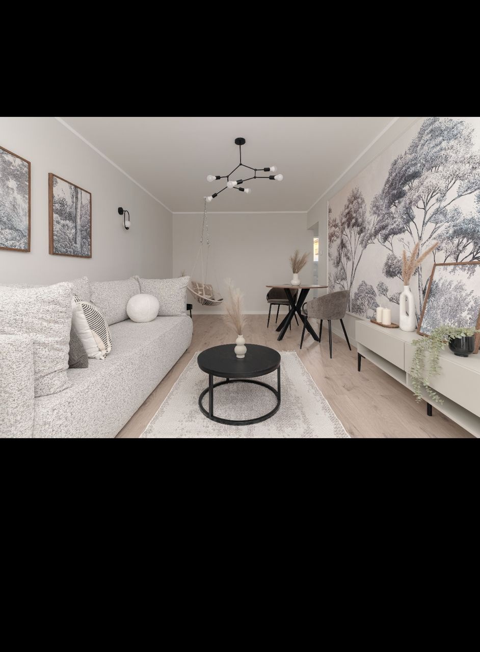 Jasne wnętrze salonu z szarą sofą, okrągłym stolikiem kawowym i fototapetą z motywem drzew. W tle wiszące krzesło i stół z krzesłami. Minimalistyczny design.