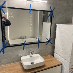 TEMIDA HOME SPÓŁKA Z OGRANICZONĄ ODPOWIEDZIALNOŚCIĄ - Nowoczesna łazienka z umywalką nablatową, lustrem w czarnej ramie zabezpieczonym taśmą malarską, pralką i suszarką Bosch w zabudowie; widoczne odbicie w lustrze przedstawia wannę i fragment osoby...