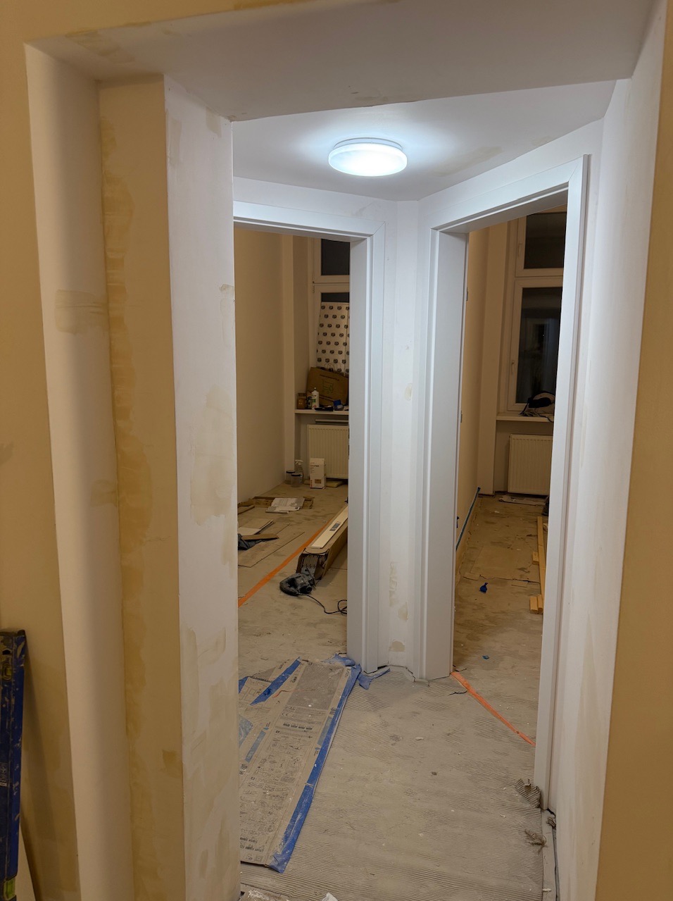 Remont wnętrza mieszkania: widok przez dwa przejścia drzwiowe. Ściany przygotowane do malowania, widoczne ślady po gładzi. Podłoga zabezpieczona folią.