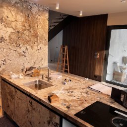 KERAM-BUD - Montaż blatu kuchennego z marmuru: widoczny zlew, płyta indukcyjna, akcesoria montażowe i drabina w tle.