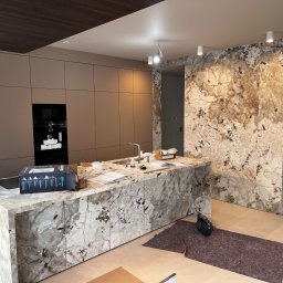 KERAM-BUD - Kuchnia w trakcie remontu: wyspa z marmurowym blatem, ściana wykończona marmurem, widoczne narzędzia i materiały budowlane, zabudowa kuchenna w tle.