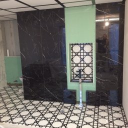 KERAM-BUD - Łazienka w trakcie wykańczania: czarne płytki imitujące marmur na ścianach, mozaika w niszy obudowanej płytą kartonowo-gipsową, wzorzysta podłoga, widoczne narzędzia i odbicie fotografa...