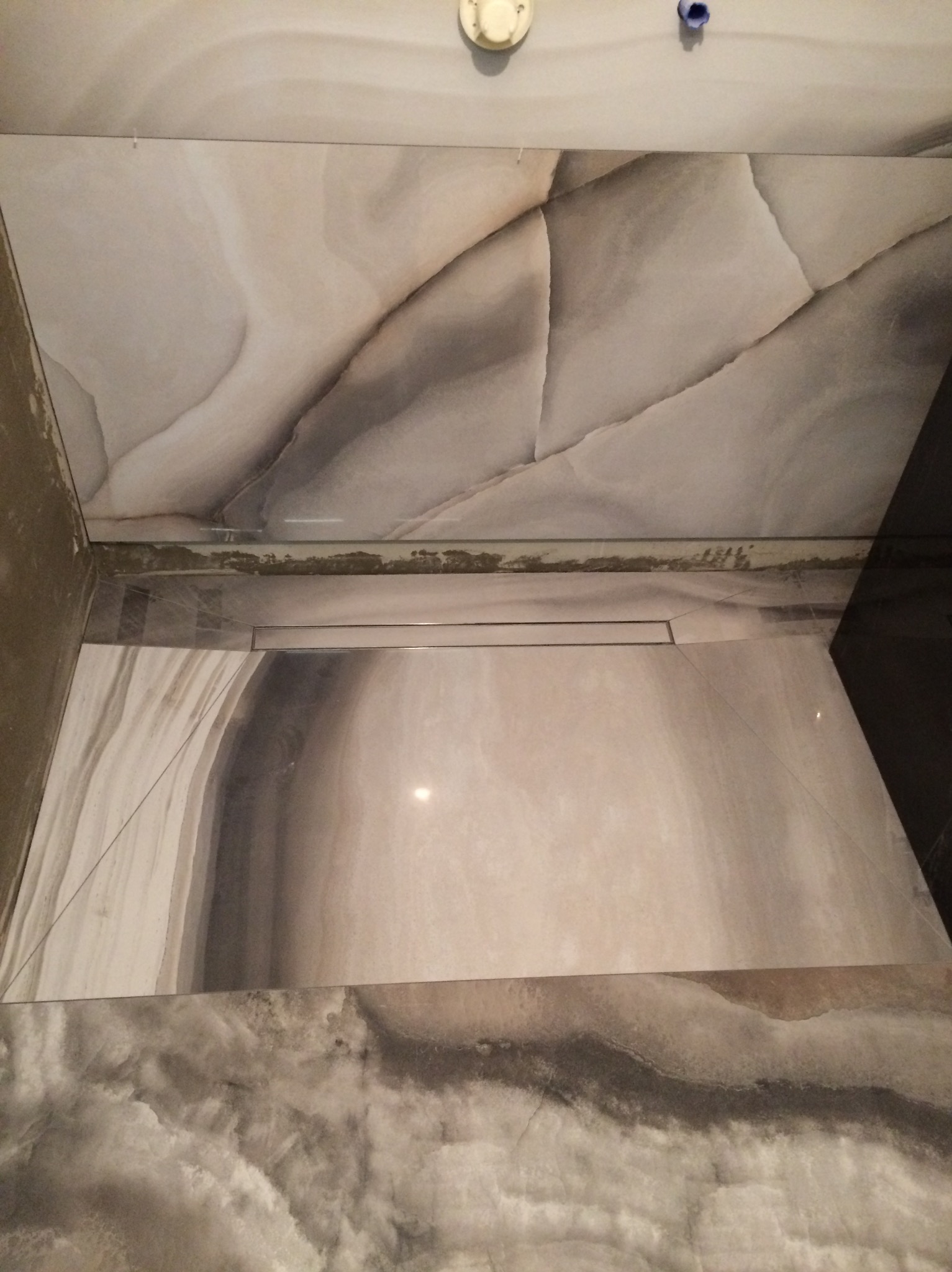 Ułożone płytki imitujące marmur na podłodze i ścianach, z widocznym odpływem liniowym, w trakcie prac wykończeniowych w łazience.