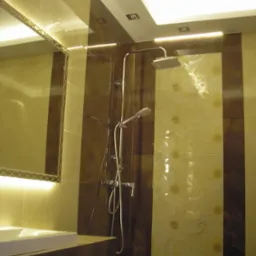 Wykończona łazienka z brązowo-beżowymi płytkami, deszczownicą i podświetlanym lustrem nad umywalką.