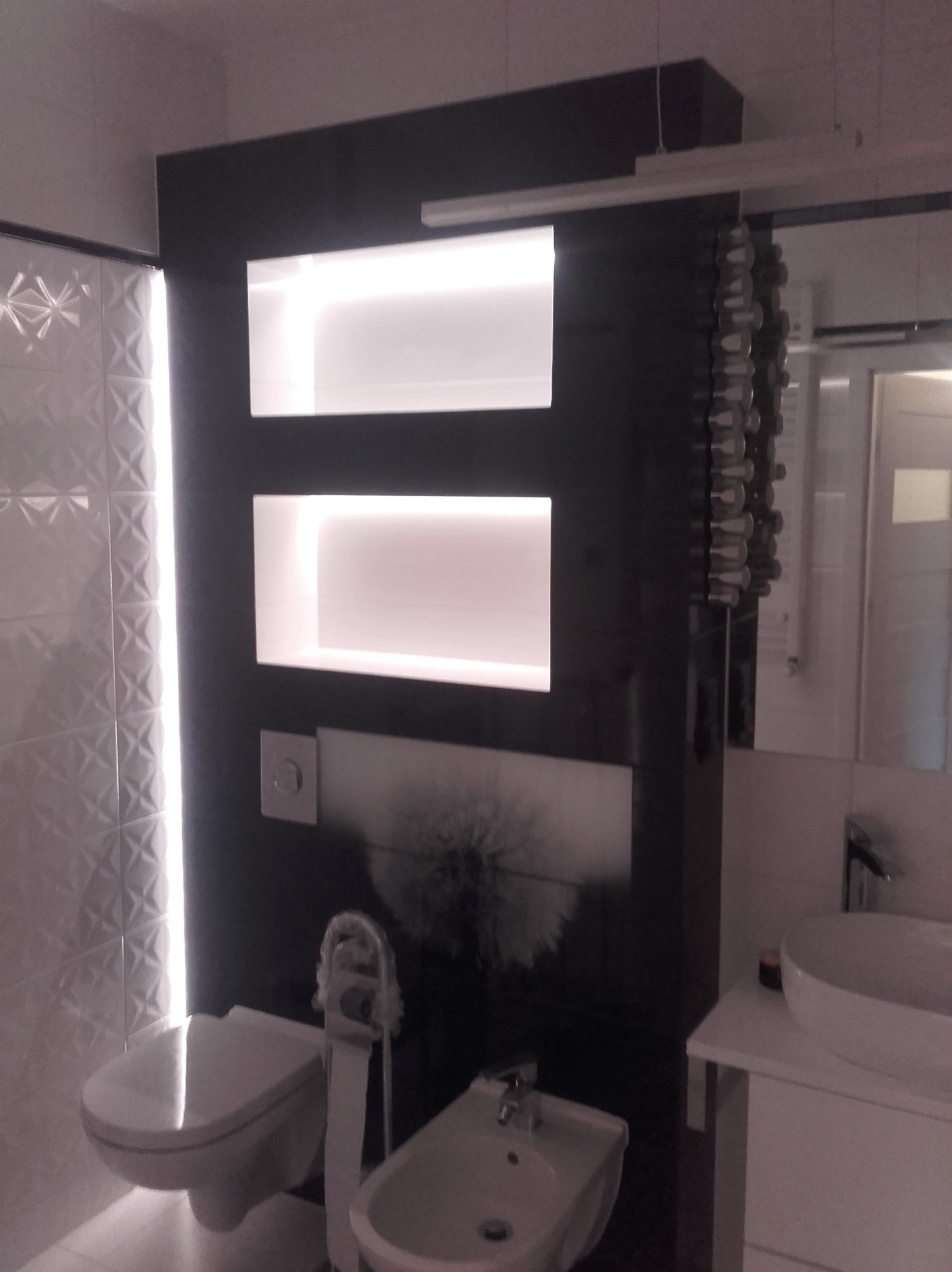 Nowoczesna łazienka z podświetlanymi półkami w zabudowie, białą armaturą i dekoracyjnymi płytkami na ścianie.