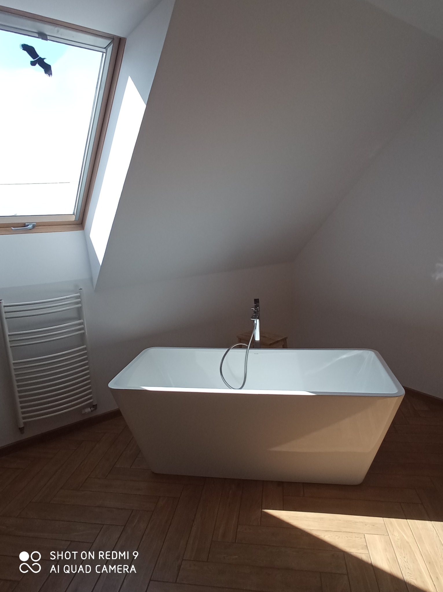 Nowoczesna, wolnostojąca wanna w łazience na poddaszu w Szczytnie, z widokiem na przelatującego ptaka przez okno dachowe.