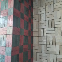 OKSANA TKACHUK - Ściana wyłożona błyszczącymi, prostokątnymi płytkami w dwóch różnych wzorach: po lewej stronie mozaika z płytek w odcieniach różu, zieleni i szarości, po prawej stronie wzór z beżowych płytek...