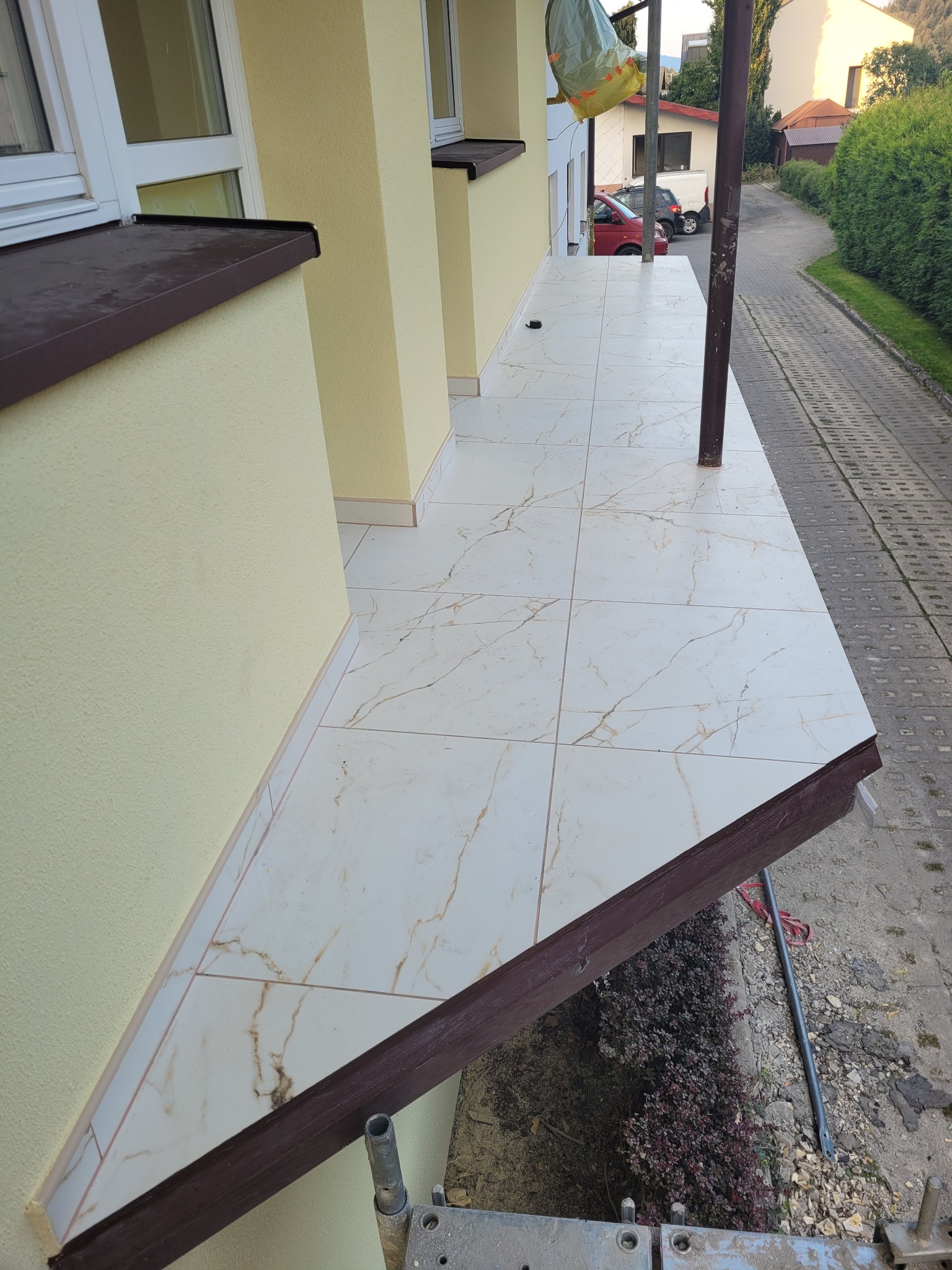 Wykończony taras z jasnymi płytkami imitującymi marmur, widok z boku, fragment rusztowania w dolnym rogu.