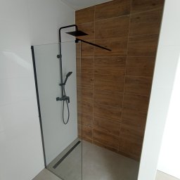 STYL DREAM HOME SPÓŁKA Z OGRANICZONĄ ODPOWIEDZIALNOŚCIĄ - Nowoczesna kabina prysznicowa walk-in z czarną armaturą i odpływem liniowym, ściany wyłożone białymi i drewnopodobnymi płytkami.