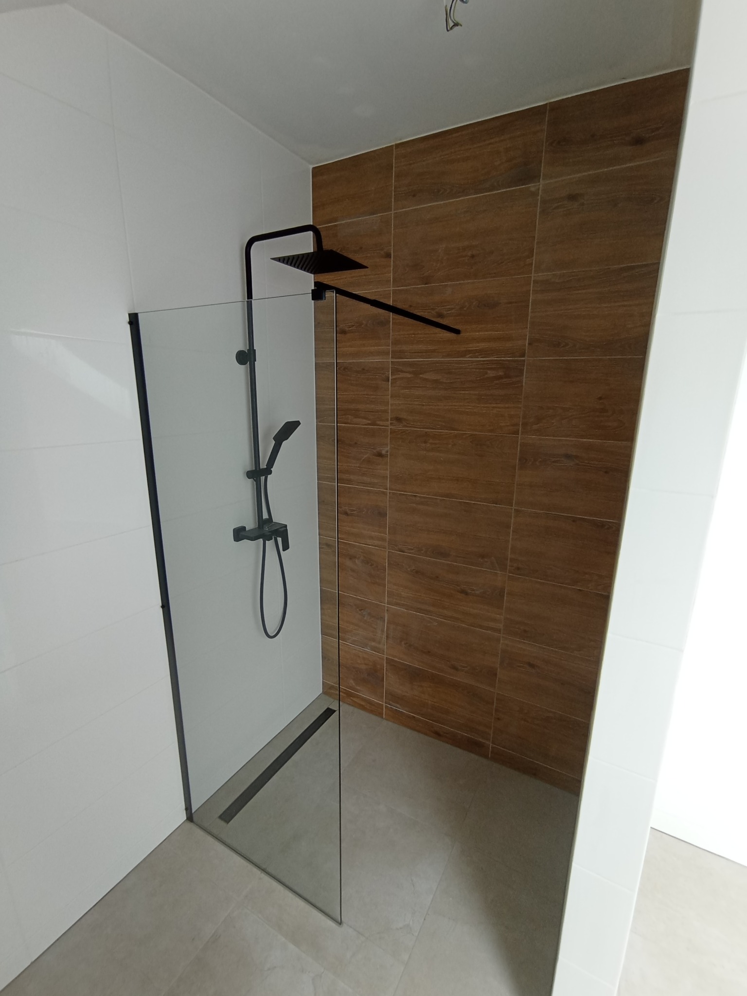 Nowoczesna kabina prysznicowa walk-in z czarną armaturą i odpływem liniowym, ściany wyłożone białymi i drewnopodobnymi płytkami.