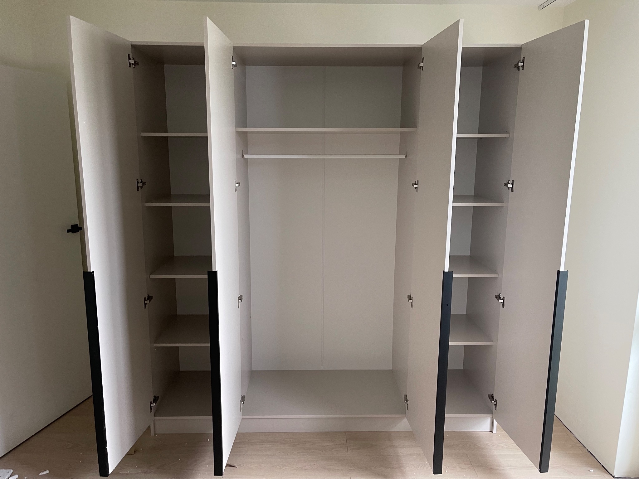 Biała szafa wnękowa z czarnymi uchwytami, szeroko otwarta, ukazująca półki i drążek na ubrania. Widok wnętrza szafy, minimalistyczny design.