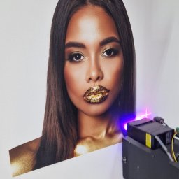 Grafic Wall - Drukarka nanosząca złoty pigment na portret kobiety z makijażem w odcieniach złota.