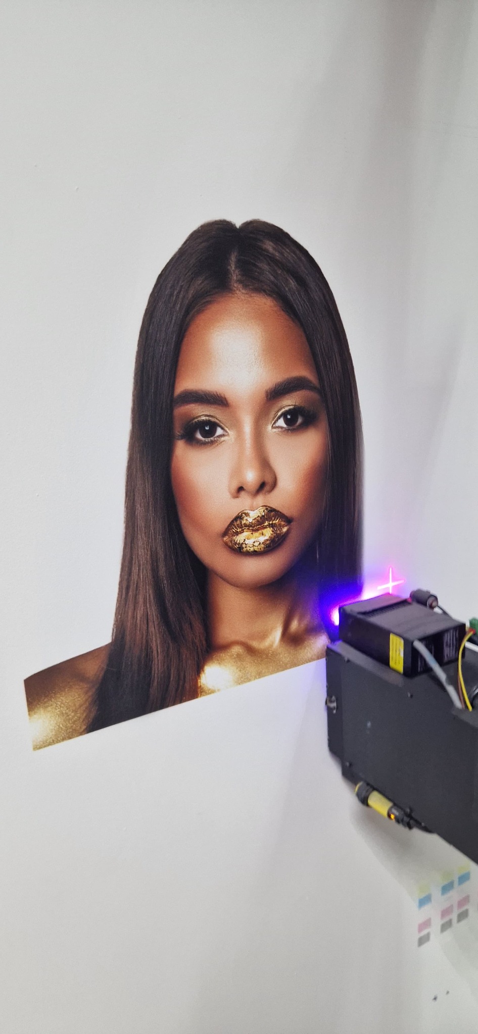 Drukarka nanosząca złoty pigment na portret kobiety z makijażem w odcieniach złota.