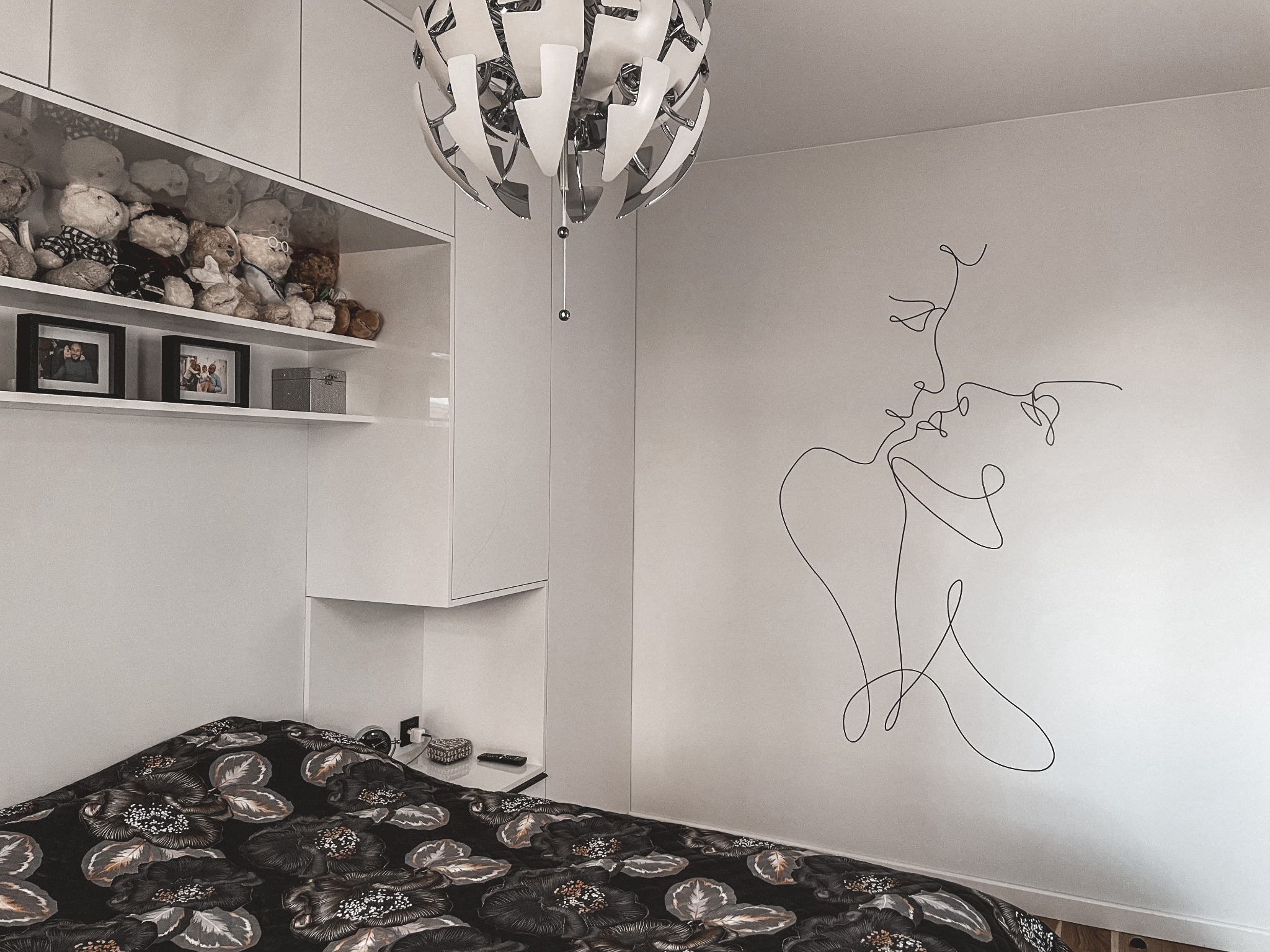 Nowoczesna sypialnia z białymi meblami w zabudowie, designerską lampą wiszącą i minimalistycznym rysunkiem linii na ścianie przedstawiającym parę całującą się.