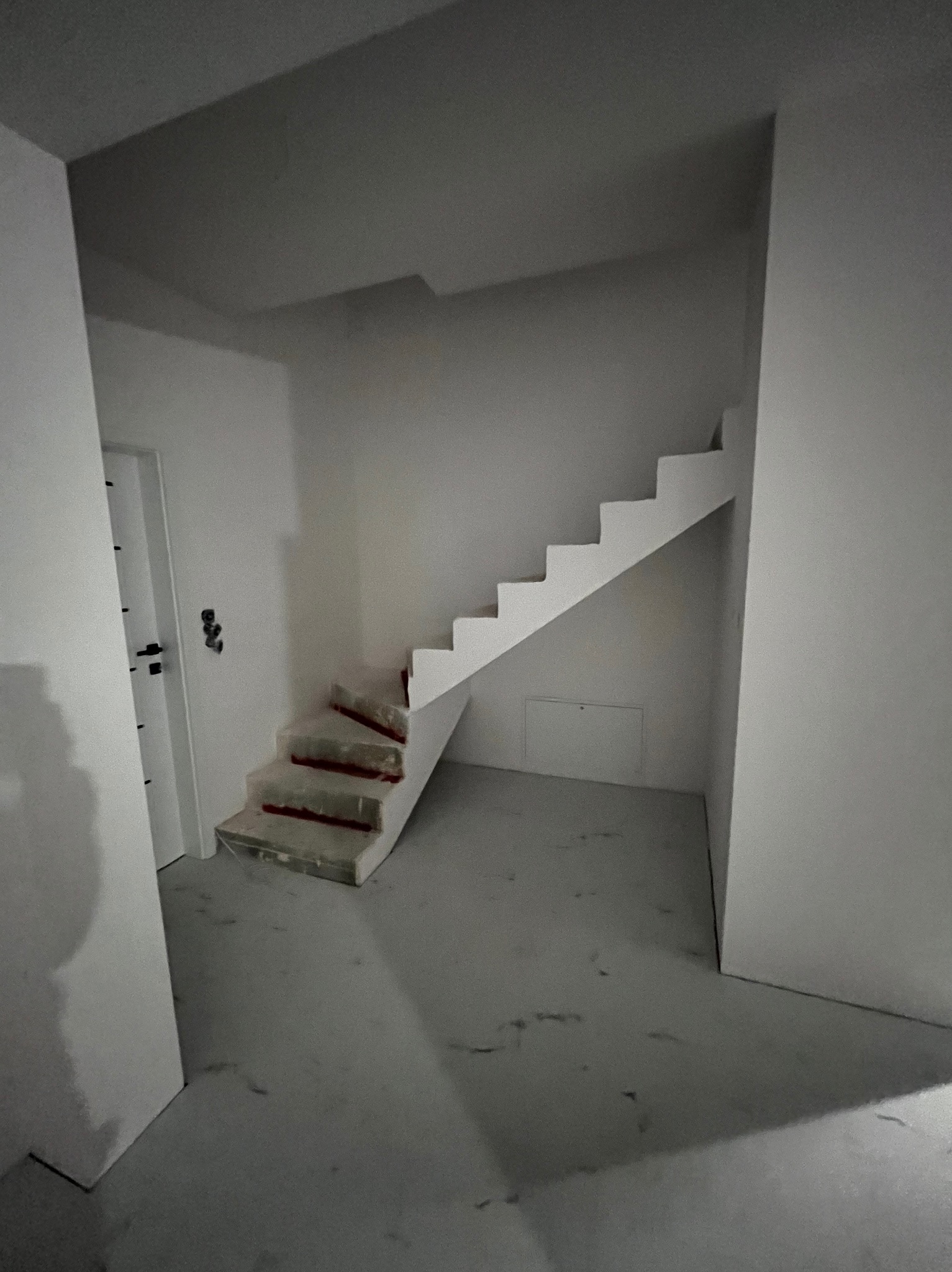 Surowe schody w trakcie prac wykończeniowych w pomieszczeniu w Warszawie, zabezpieczone folią, widoczne ślady po pracach na podłodze i ścianach, przygotowane do dalszych etapów prac.