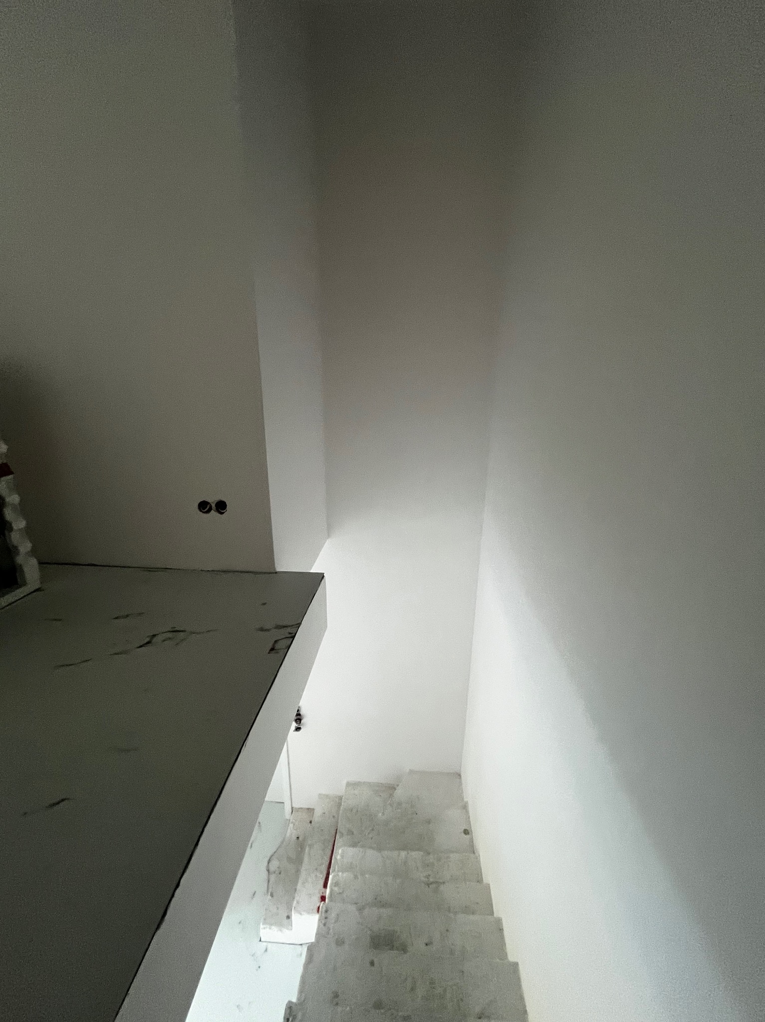 Wnętrze w trakcie prac wykończeniowych: białe ściany, schody w stanie surowym, widoczne puszki elektryczne, fragment konstrukcji z płyty.