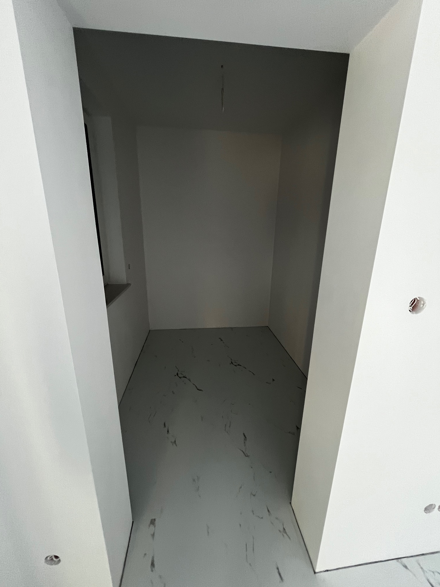 Pusty pokój po szpachlowaniu i położeniu podłogi imitującej marmur, widoczny otwór na gniazdko elektryczne na ścianie.