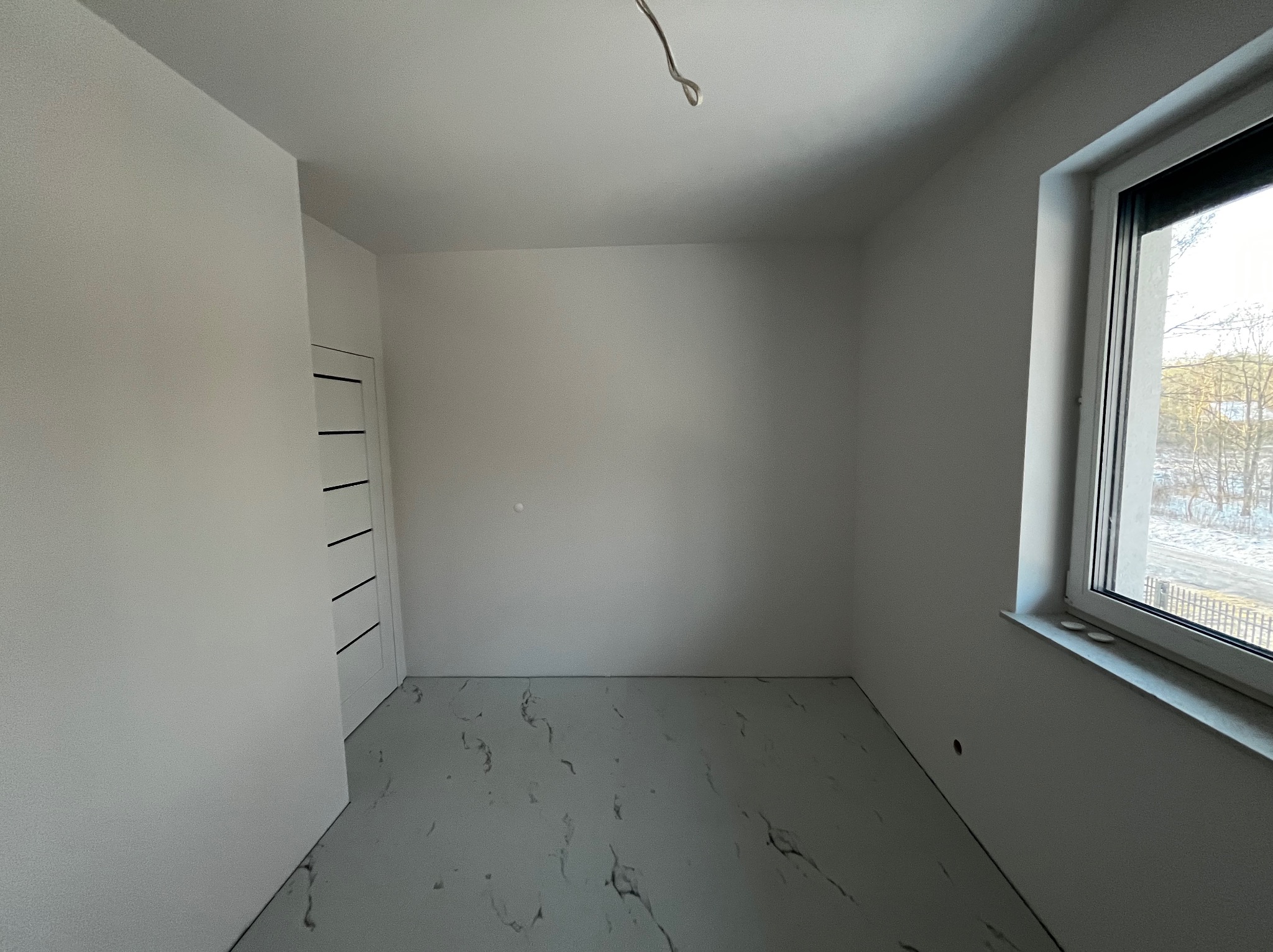 Pusty, jasny pokój po remoncie z marmurową podłogą, białymi ścianami i nowymi drzwiami z czarnymi akcentami, widok z okna na zimowy krajobraz.