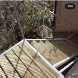 Metalowa konstrukcja schodów z drewnianymi stopniami, widok z góry, w tle kwitnące drzewo.