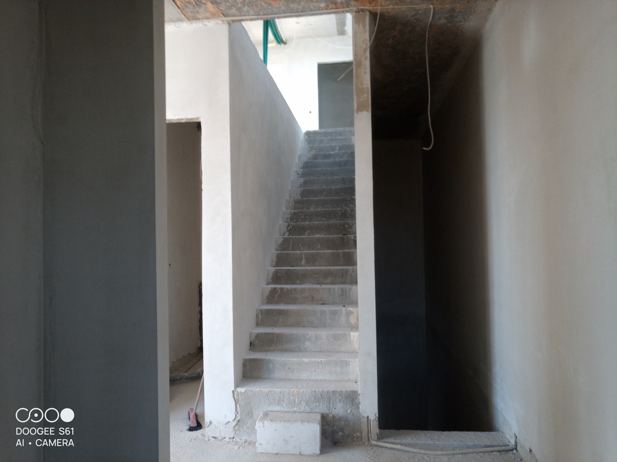 Surowe, otynkowane schody betonowe w surowym stanie, prowadzące na wyższą kondygnację, z widocznymi niedoskonałościami i przerwami w tynku.