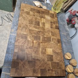 Tymoteusz Berny - Surowy blat drewniany z mozaiką z kwadratowych klocków, leżący na warsztatowym stole, obok widoczne niedokończone elementy i narzędzia, sugerujące etap produkcji.