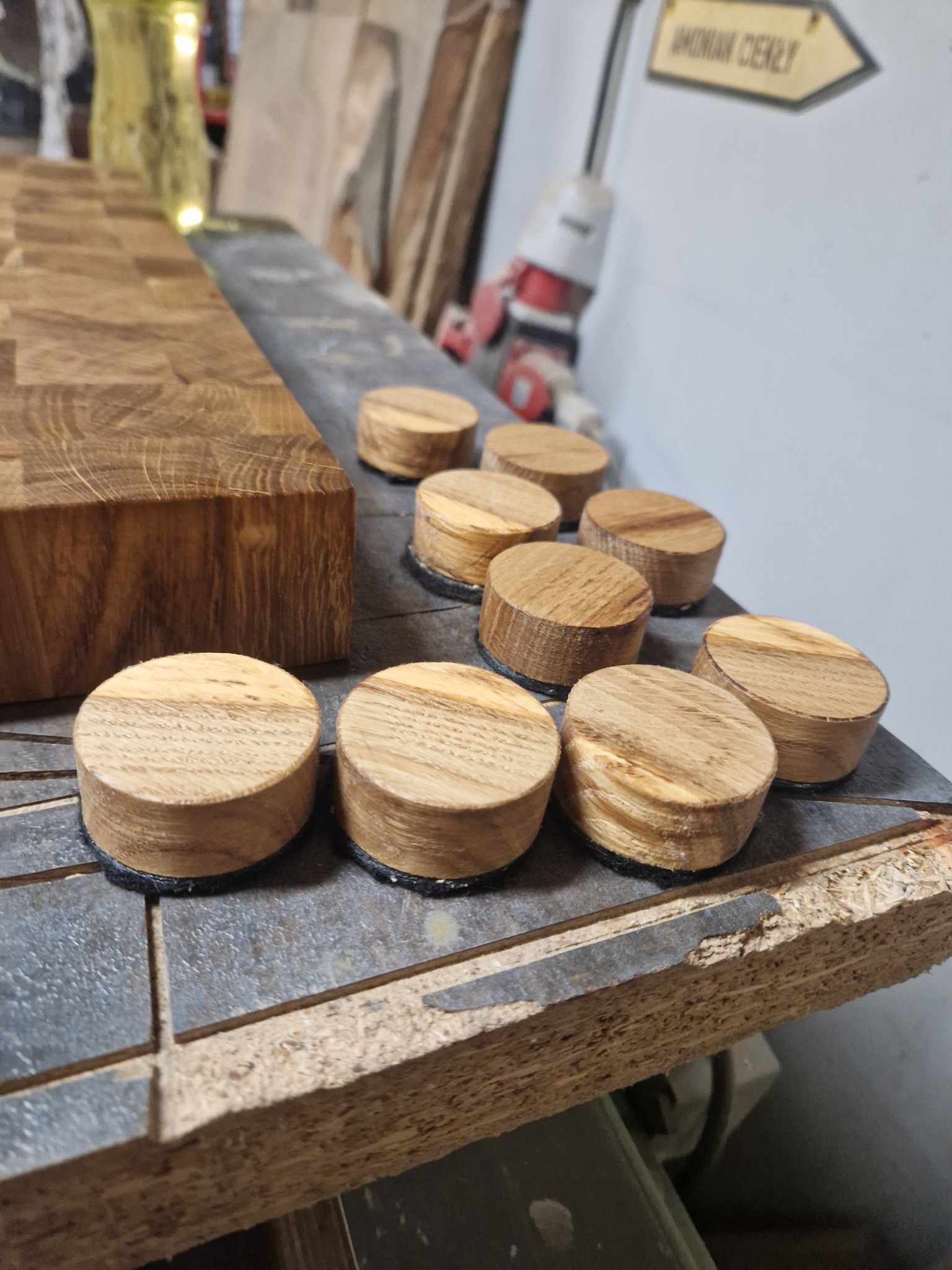 Drewniane, okrągłe podkładki z filcem u podstawy, ułożone na blacie roboczym obok drewnianego klocka z widocznymi słojami.