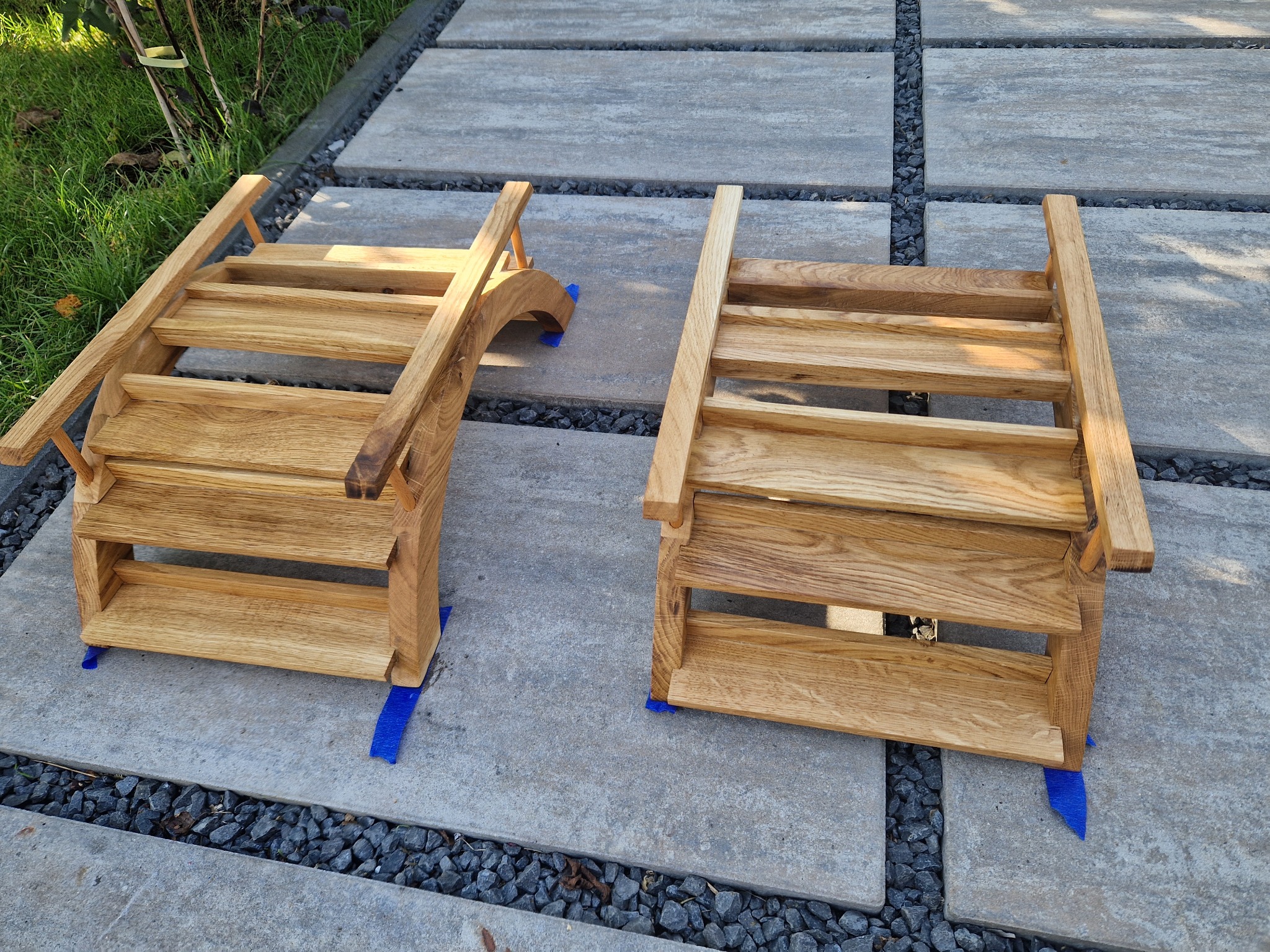 Dwa drewniane podesty schodkowe, wykonane z jasnego drewna, ustawione na betonowych płytach z kamienną podsypką; jeden z podestów ma zaokrąglony bok, oba zabezpieczone niebieską taśmą.
