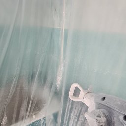 Osthouse - Łazienka zabezpieczona folią malarską, w kadrze fragment pistoletu natryskowego Graco, ślady farby na urządzeniu.