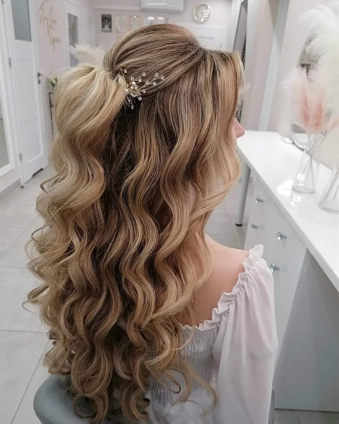 Blond włosy upięte w fale, ozdobione delikatną spinką z kryształkami, widok z boku w salonie.