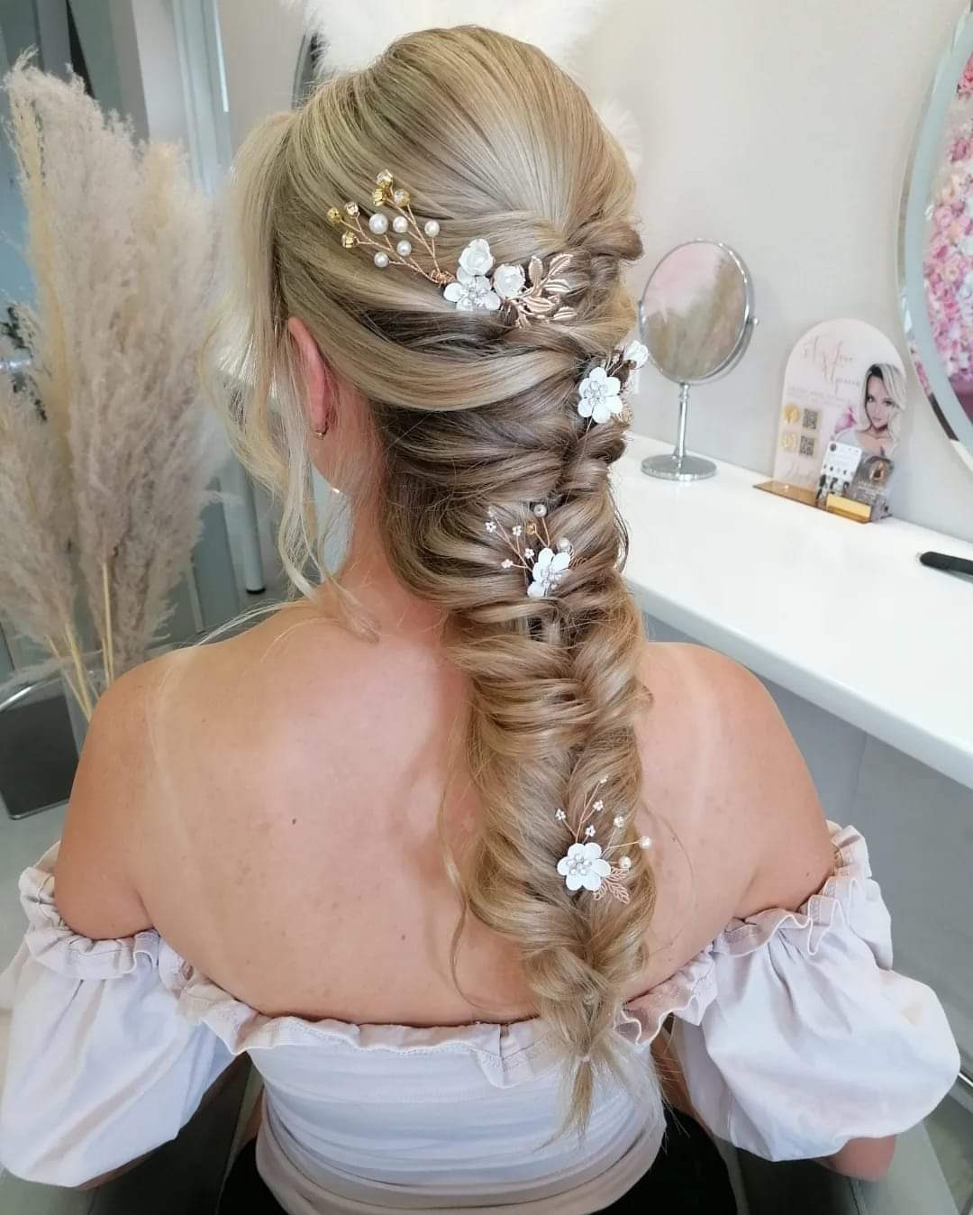 Blond włosy upięte w gruby warkocz z ozdobami kwiatowymi i perłami, widok z tyłu, bluzka z odkrytymi ramionami