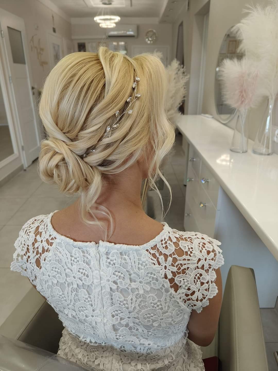 Upięcie blond włosów z ozdobną spinką z tyłu głowy, widoczny koronkowy top sukienki.