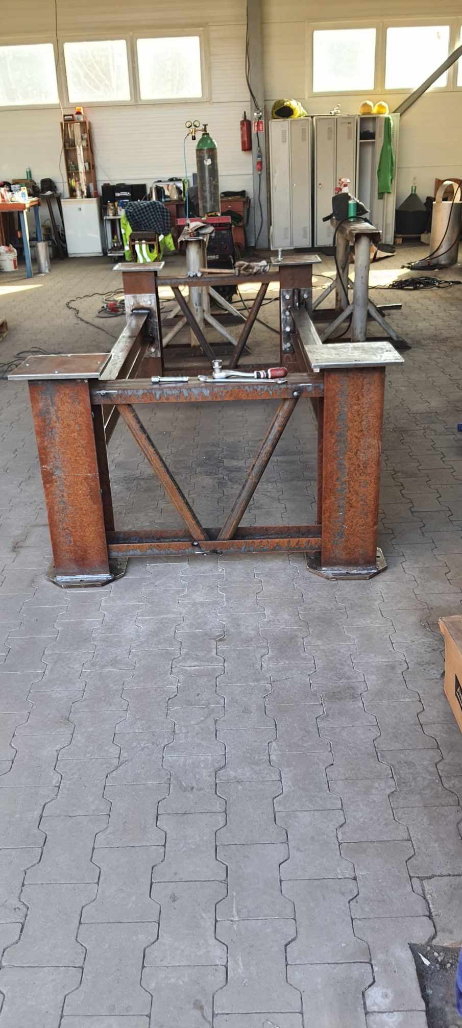 Konstrukcja stalowa z profili i rur, spawana, z widocznymi śladami korozji, w warsztacie, z narzędziami na górnej powierzchni.