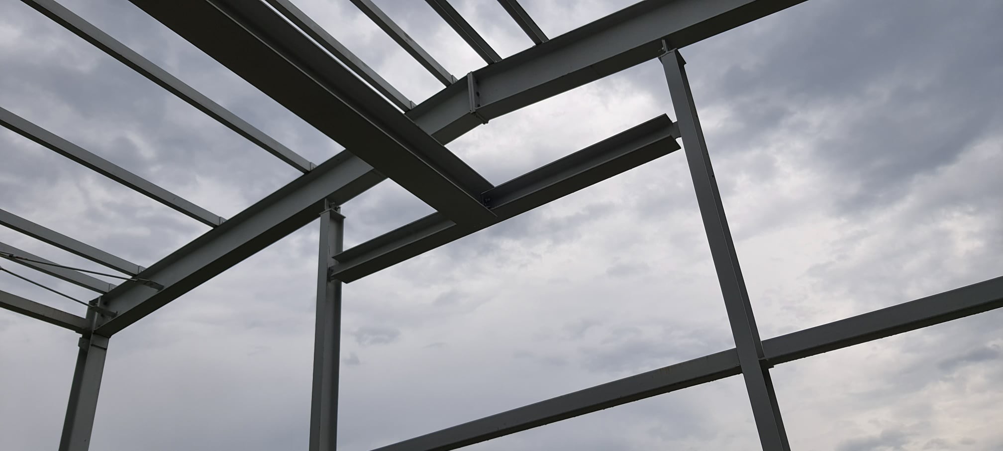 Stalowa konstrukcja hali w trakcie budowy, widoczne elementy szkieletu na tle pochmurnego nieba.