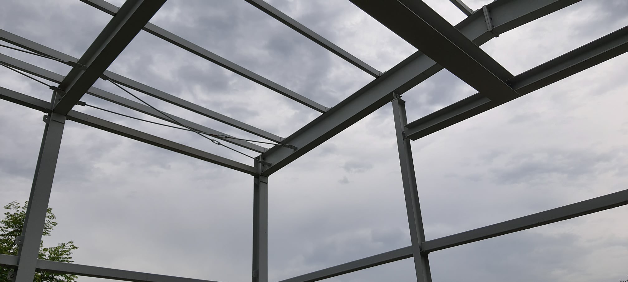 Konstrukcja stalowa hali w trakcie budowy, widok z dołu na szkielet z belek i słupów, pochmurne niebo w tle.