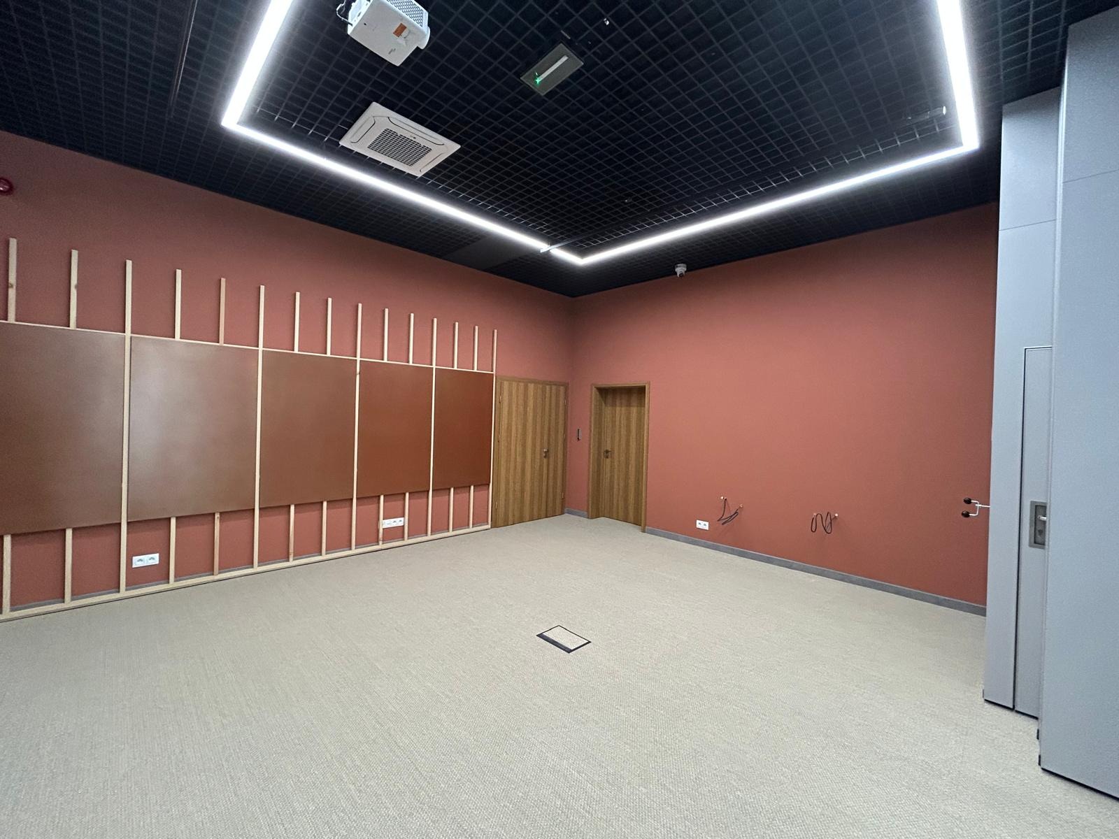 Wykończone wnętrze biurowe: terakotowe ściany, panele dekoracyjne, jasna wykładzina dywanowa, podwieszany sufit z oświetleniem LED i klimatyzacją.