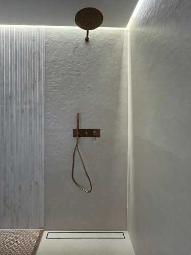 Nowoczesna kabina prysznicowa z deszczownicą w odcieniach bieli i miedzi. Minimalistyczny design, oświetlenie LED, odpływ liniowy. Eleganckie wykończenie.