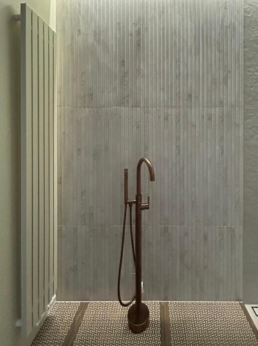 Nowoczesna łazienka z wolnostojącą baterią w kolorze miedzi, dekoracyjną ścianą z płytek i grzejnikiem drabinkowym. Uwagę przykuwa wzór na podłodze.