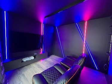 Nowoczesne kino domowe: czarne ściany, podświetlenie LED (róż, niebieski), skórzane fotele z pikowaniem, drewniana podłoga. Minimalistyczny design, unikalne oświetlenie.