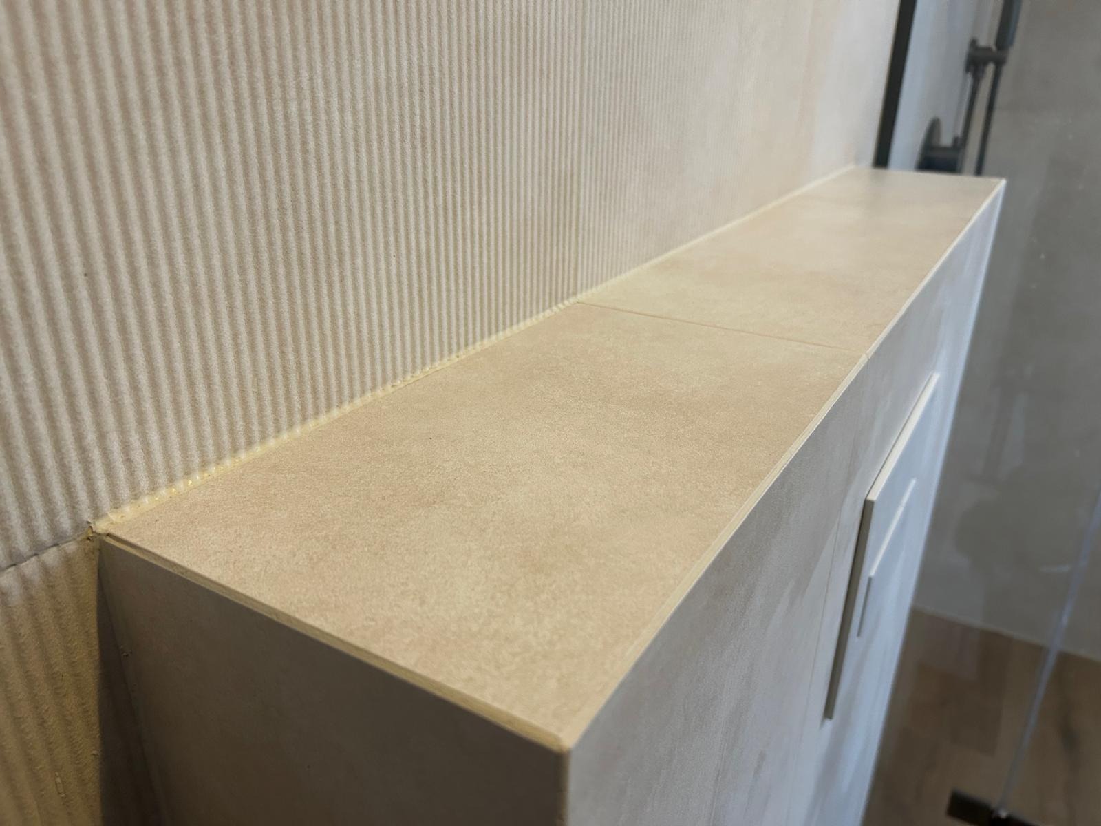 Beżowa półka z płytek w łazience, z widoczną teksturą ściany i fugą. Minimalistyczny design, ciepłe odcienie, nowoczesne wykończenie.