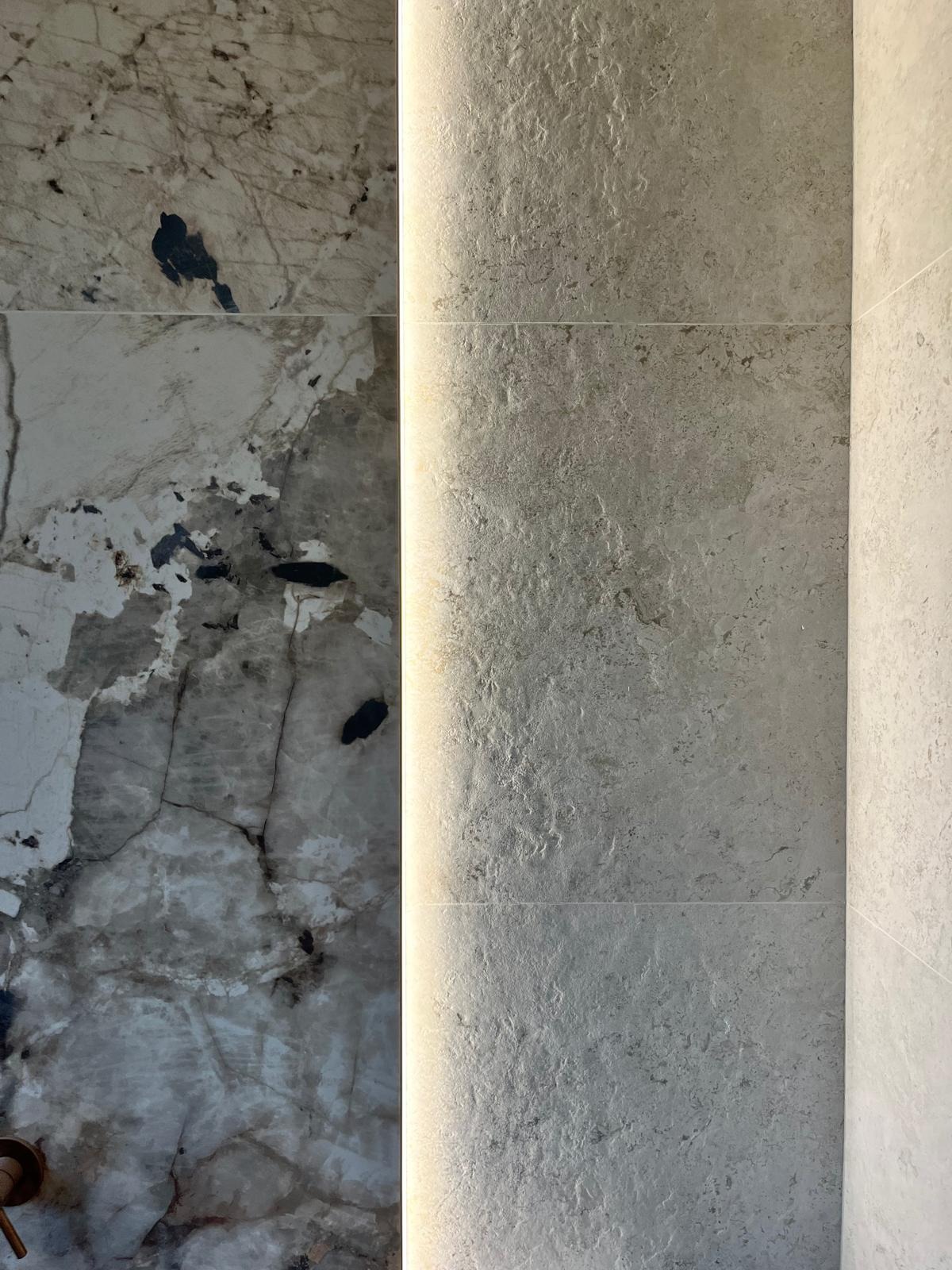 Ściana wyłożona płytkami z marmurowym wzorem i oświetleniem LED, ukazująca detale faktury i połączenie materiałów w aranżacji wnętrza.